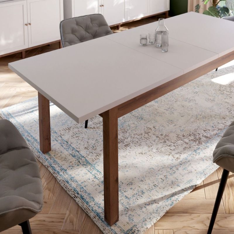 Extending white Dining table with wooden legs and a gray top in a room with chairs and a rug.
