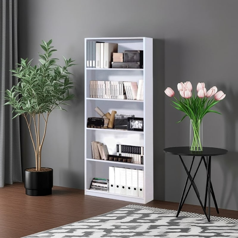 White bookshelf with books, a plant, and a vase of flowers in a room with a gray wall and wooden floor.