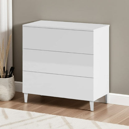 White dresser with three drawers against a beige wall.