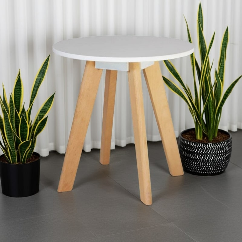 Small round table with wooden legs and a white top, flanked by two potted plants against a white curtain background.