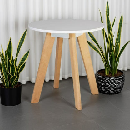 Small round table with wooden legs and a white top, flanked by two potted plants against a white curtain background.