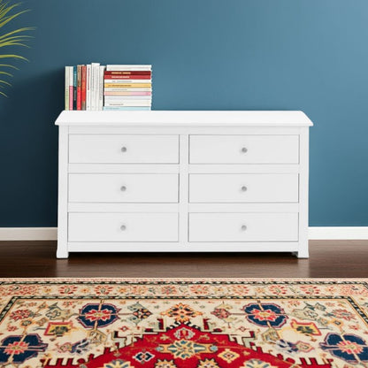 White dresser with 6 drawers and books against a blue wall with a patterned rug on the floor.