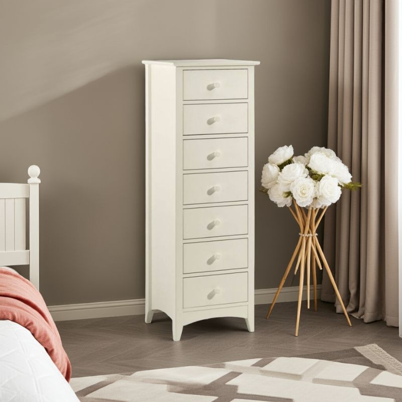 White tall chest of drawers in a bedroom with a vase of white flowers on a wooden stand.
