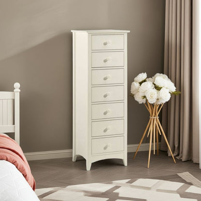 White tall chest of drawers in a bedroom with a vase of white flowers on a wooden stand.