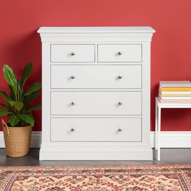 White dresser with multiple drawers against a red wall, with a plant and books on a small table in the foreground.