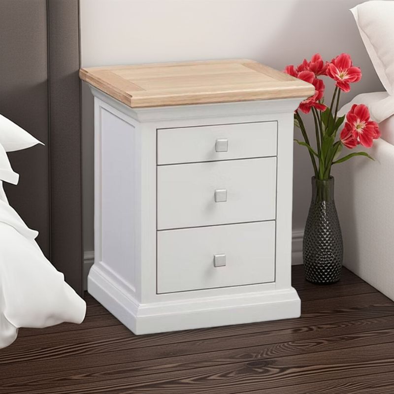 White nightstand with wooden top next to a vase of red flowers on a wooden floor.