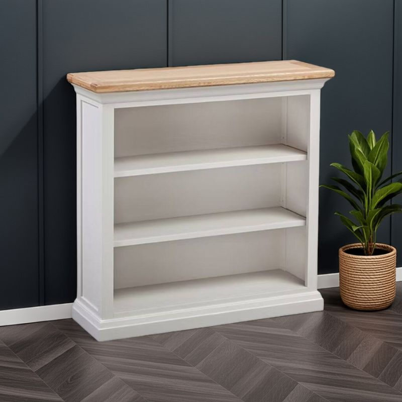 White bookshelf with wooden top against a dark paneled wall with a plant on the floor.