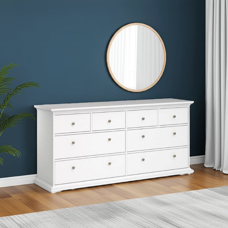 White dresser with round mirror against a blue wall in a room with wooden flooring.