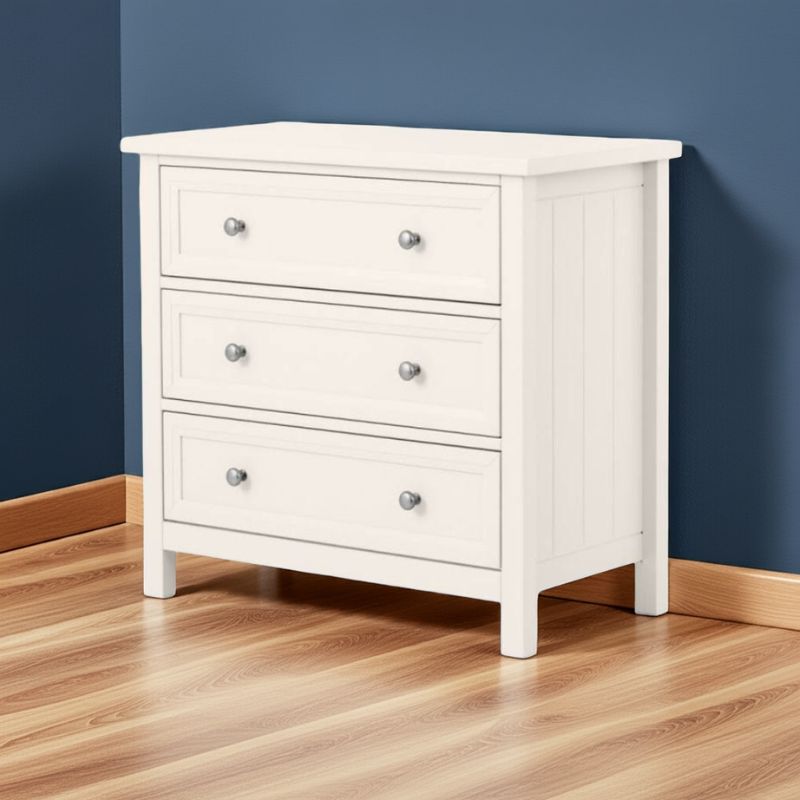 White dresser with three drawers against a blue wall on a wooden floor