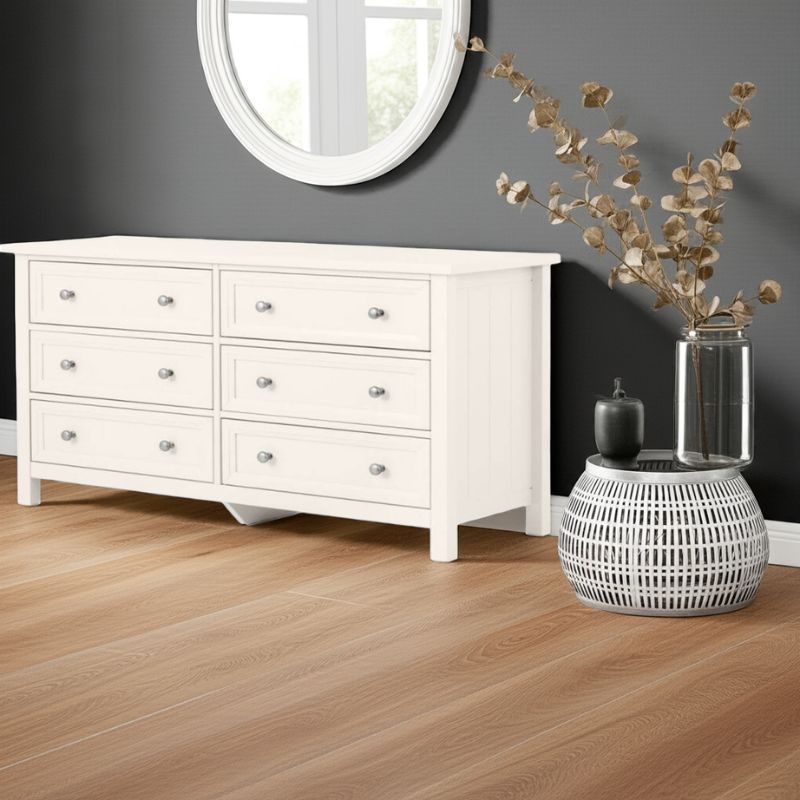 White dresser with decorative items on a wooden floor against a gray wall.