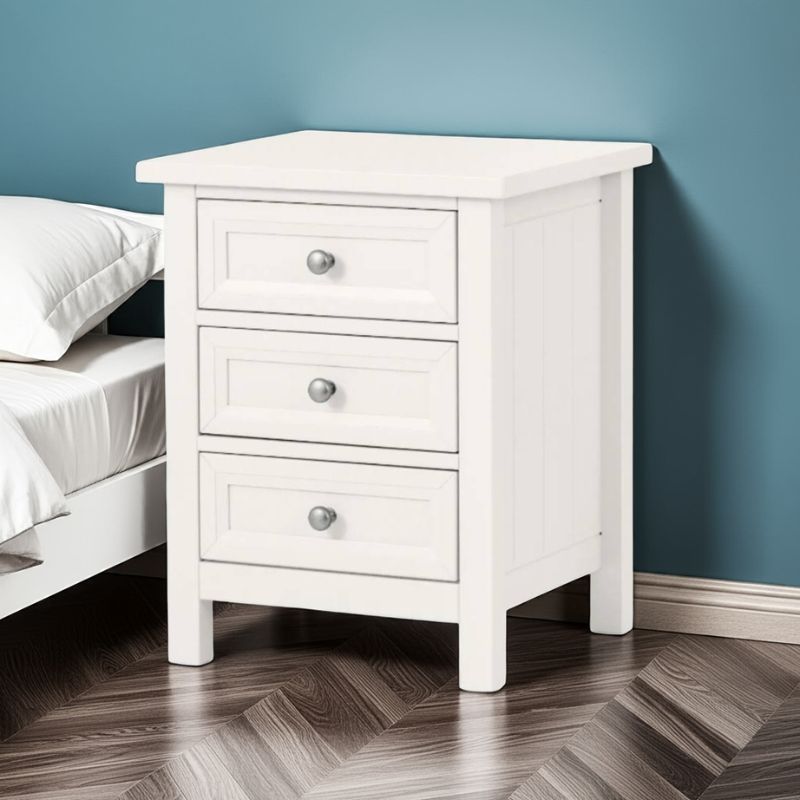 White nightstand with three drawers against a blue wall.