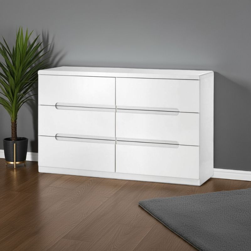 White dresser with four drawers against a gray wall with a plant on the left.