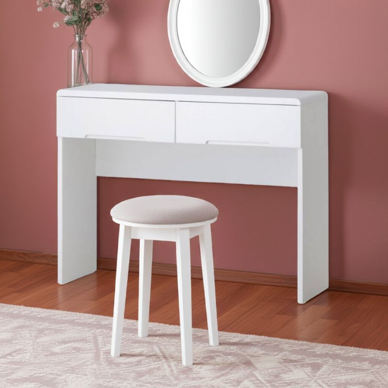 White vanity table with a mirror and stool against a pink wall.