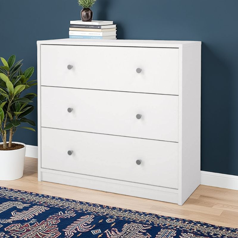 White dresser with three drawers against a blue wall, with a plant and books on top.