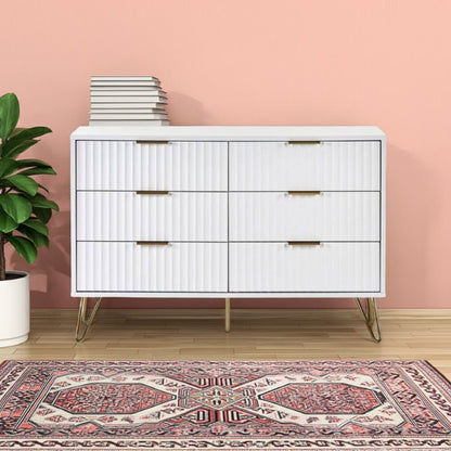 White dresser with gold handles against a pink wall with a plant and rug.