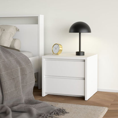 White nightstand with black lamp and gold clock next to a bed in a bedroom.