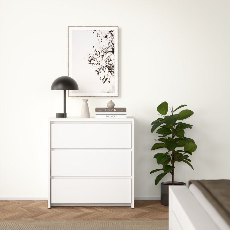White dresser with decorative items and a plant in a minimalistic room.