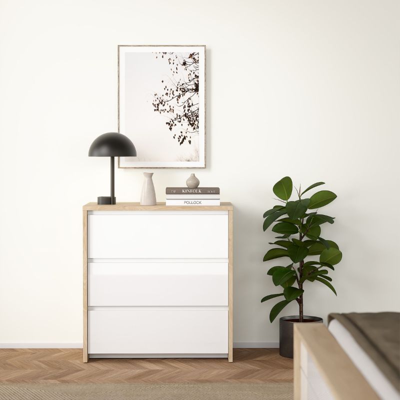 White dresser with wooden frame, black lamp, and plant in a minimalistic room.