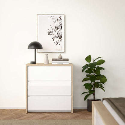 White dresser with wooden frame, black lamp, and plant in a minimalistic room.