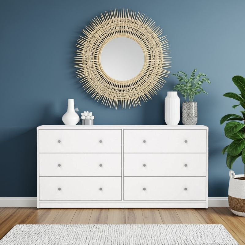 White dresser with 6 large drawers with decorative items against a blue wall
