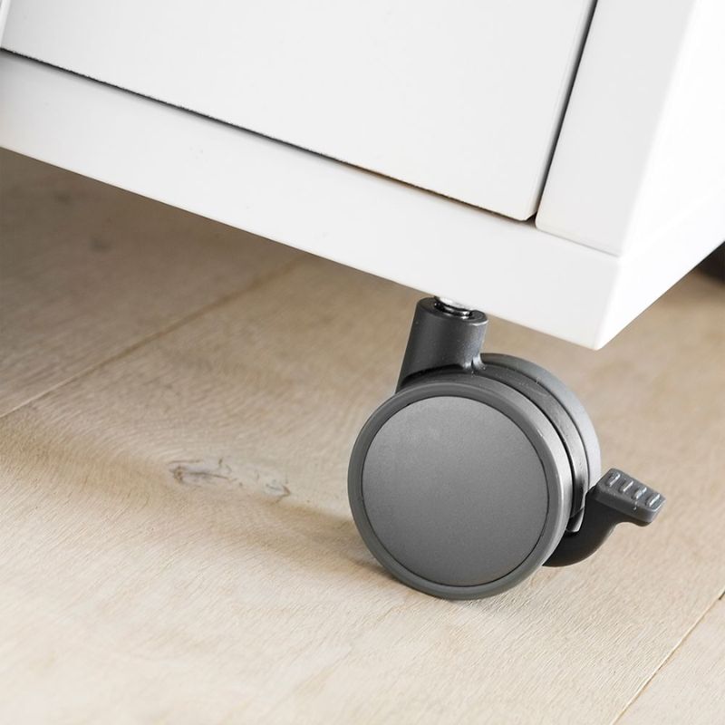 Gray caster wheel on a wooden floor with a white cabinet in the background