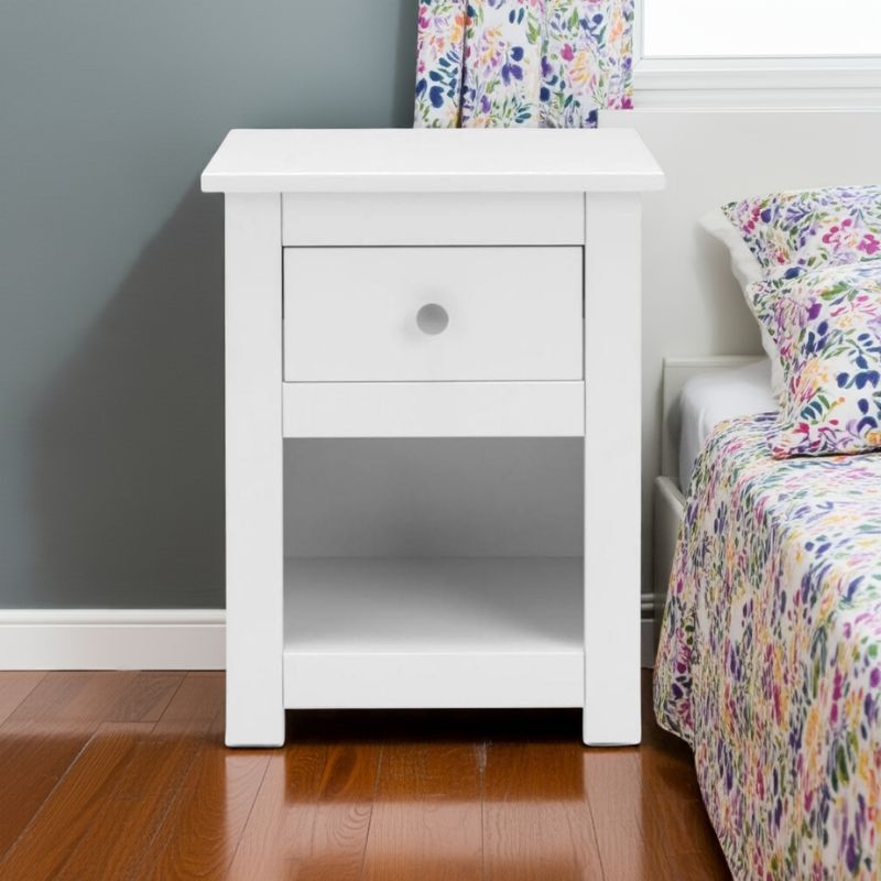 White nightstand next to a bed with colorful bedding in a bedroom setting.