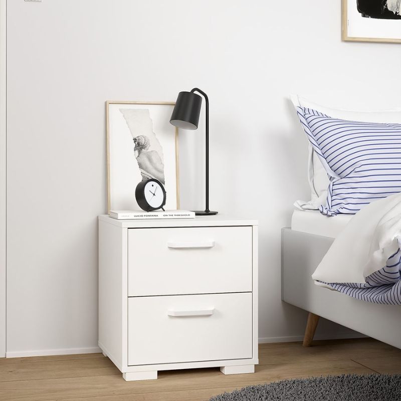 White nightstand with a lamp and clock next to a bed with striped pillows.
