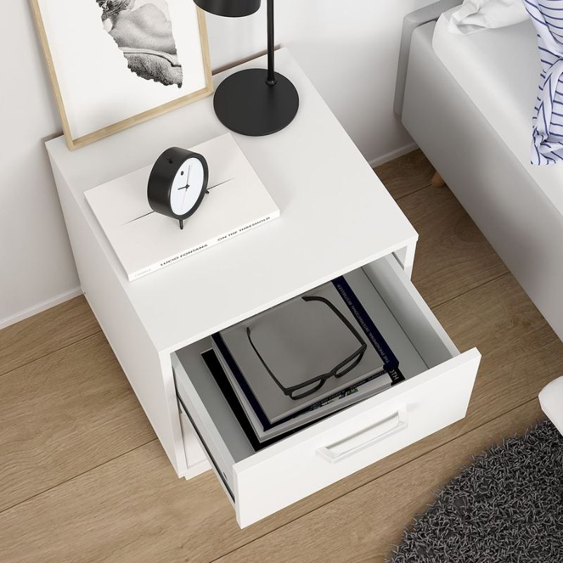 White nightstand with open drawer, clock, and book on top in a bedroom setting.