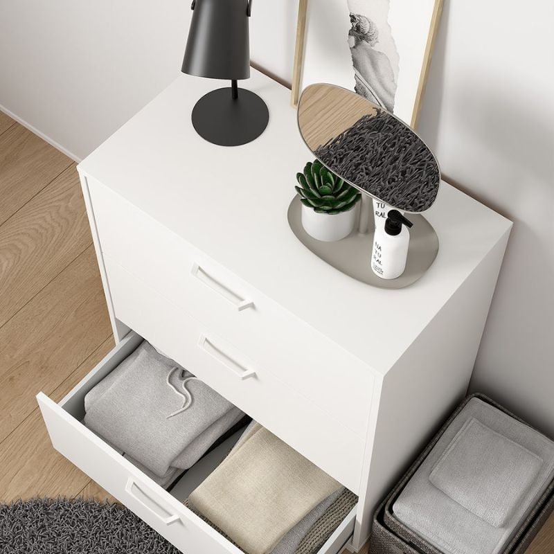 White dresser with open drawer containing folded clothes, a lamp, plant, and bottle on top.