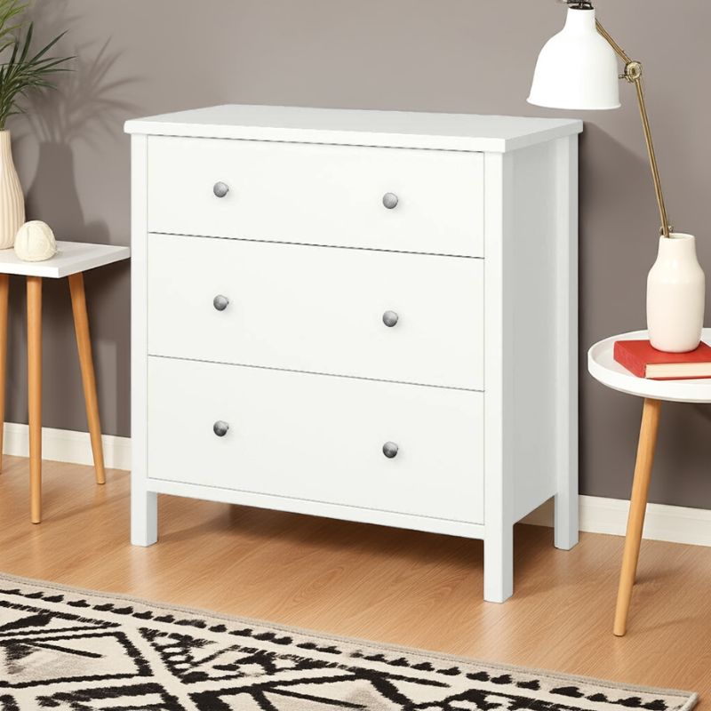 White dresser with gray knobs in a room with a lamp, plant, and small table.