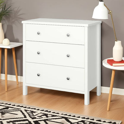 White dresser with gray knobs in a room with a lamp, plant, and small table.