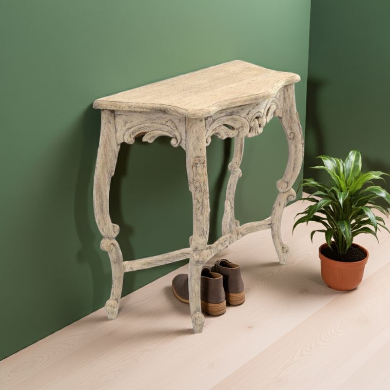 French styled vintage console table against a green wall with a plant and shoes on a beige floor.
