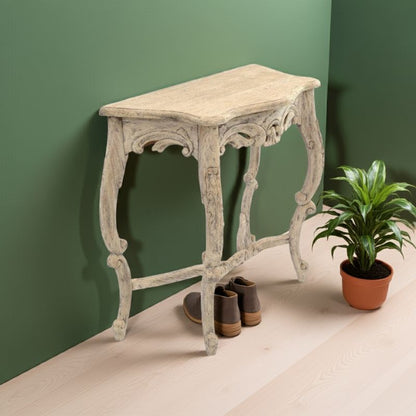 French styled vintage console table against a green wall with a plant and shoes on a beige floor.