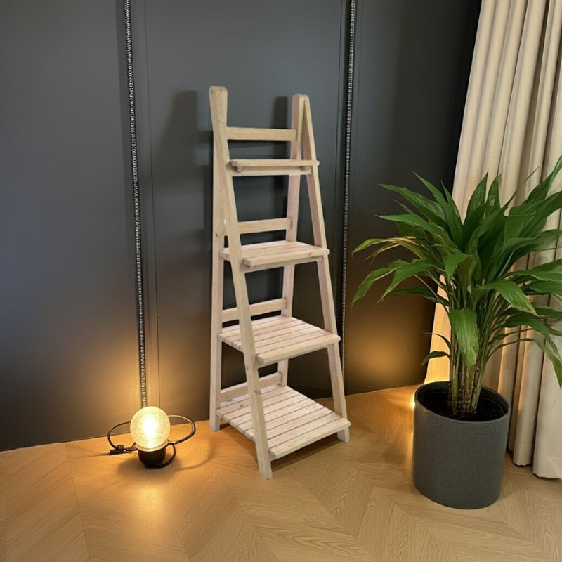Wooden ladder shelf against a dark wall with a plant and lamp on a wooden floor.