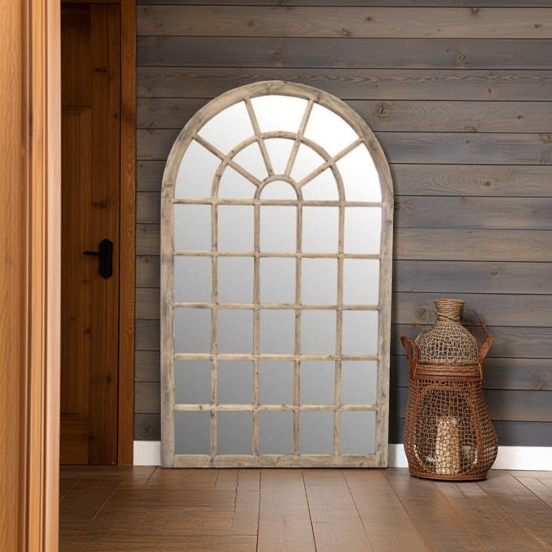 Arched window-style mirror with rustic frame against a wooden wall.