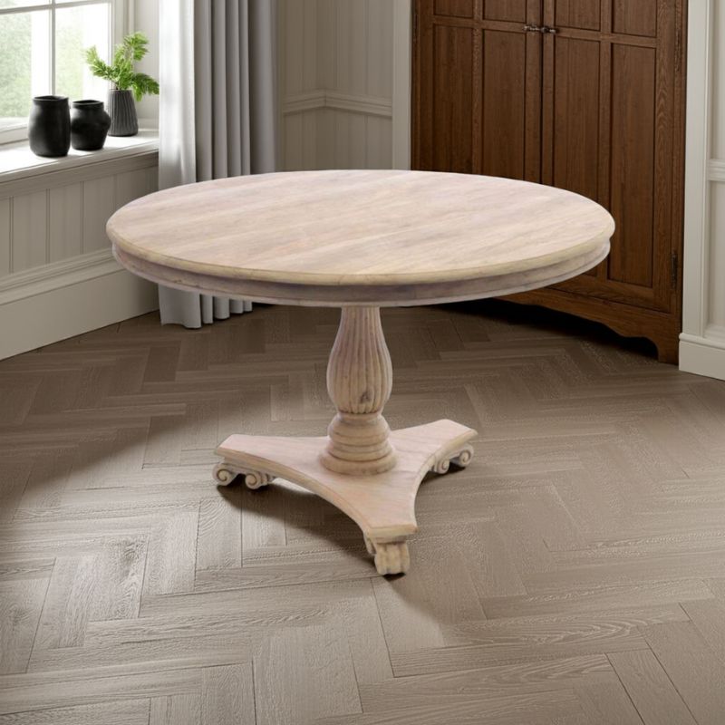 Round wooden table with a pedestal base in a room with wooden flooring and a window.
