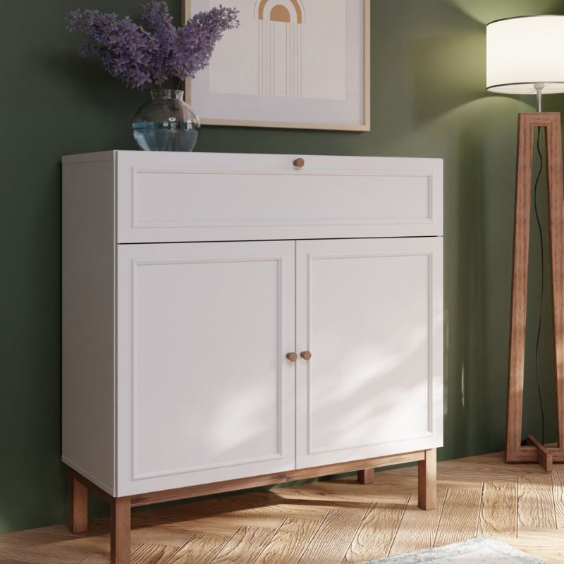 White cabinet with wooden legs against a green wall with a lamp and framed picture.