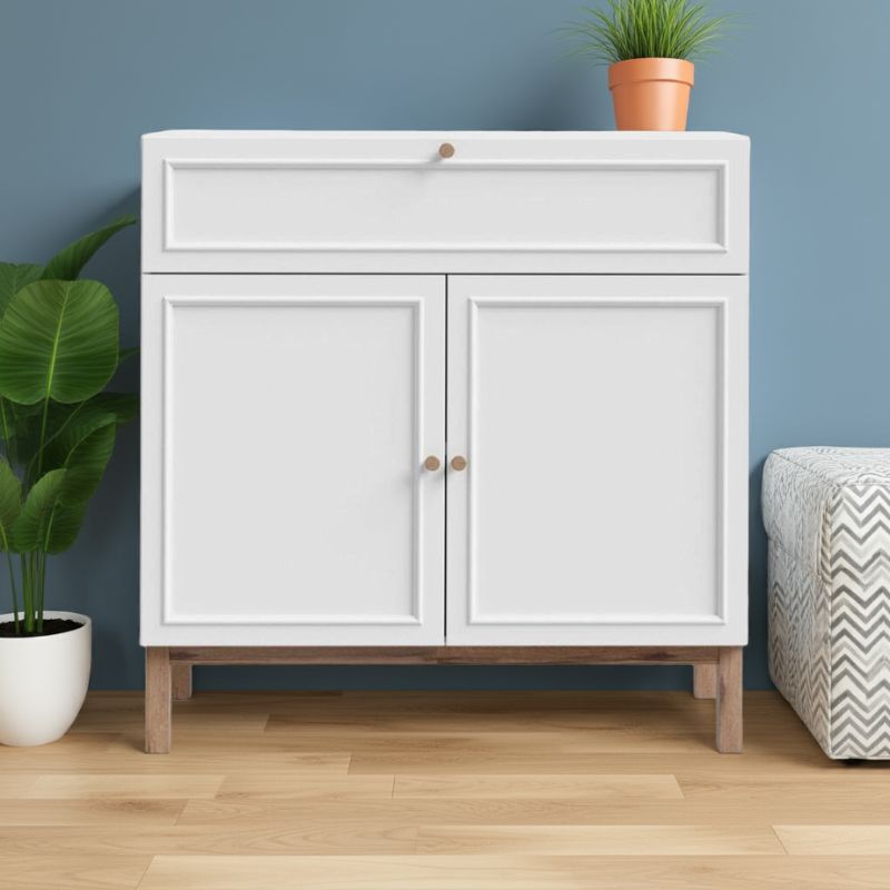 White cabinet with wooden legs against a blue wall with plants and a cushion.