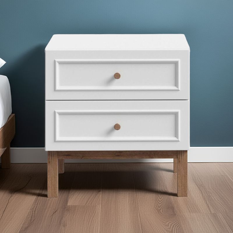 White nightstand with wooden legs against a blue wall