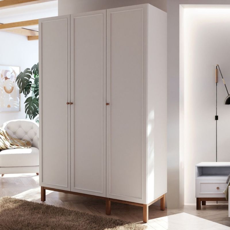 White triple wardrobe with wooden legs in a room with a sofa and lamp.