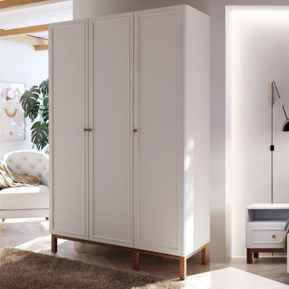 White triple wardrobe with wooden legs in a room with a sofa and lamp.