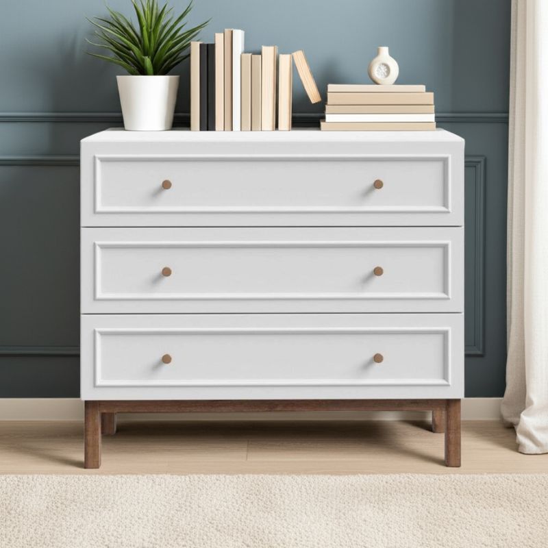 White dresser with wooden legs and drawers, decorated with books and a plant, against a blue wall.