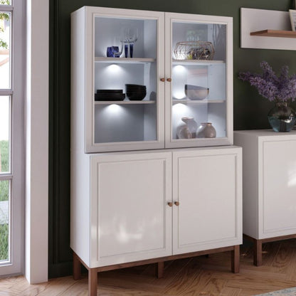 White display cabinet with glass doors in a room with a window and another piece of furniture.
