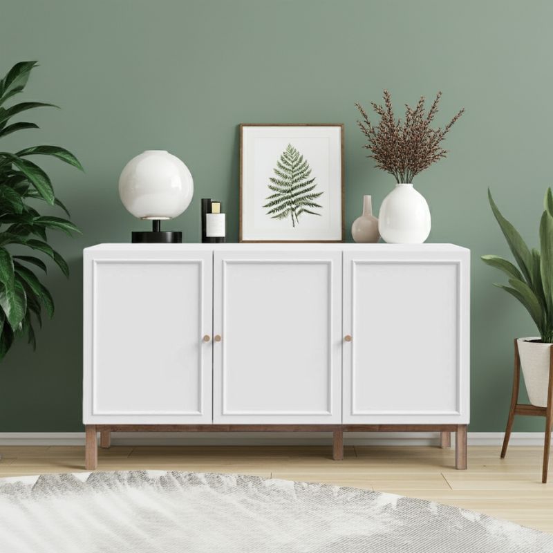 White sideboard with 3 doors with decorative items against a green wall