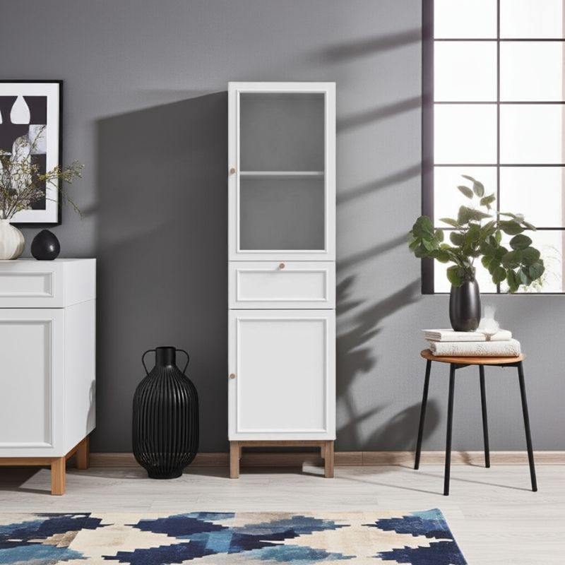 White narrow display cabinet in a room with a gray wall, black vase, and a small table with a plant.