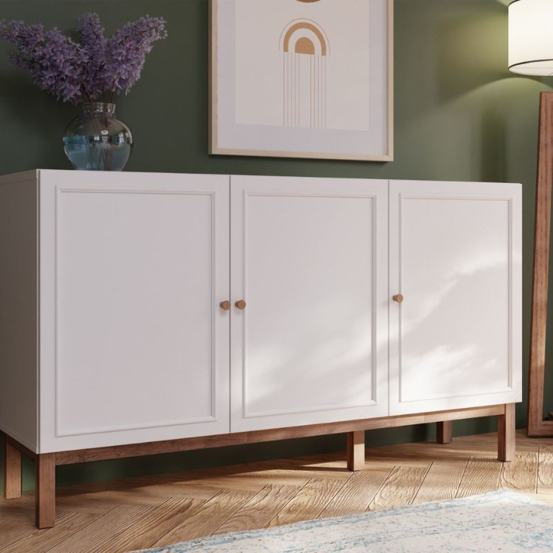 White sideboard with wooden legs against a green wall with a painting and vase of purple flowers.