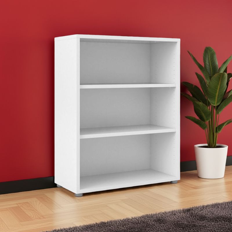 Small White bookshelf with three shelves against a red wall with a plant on a wooden floor.